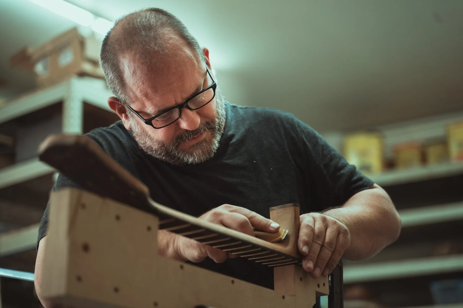 A craftsperson working on a guitar neck held in a wooden jig